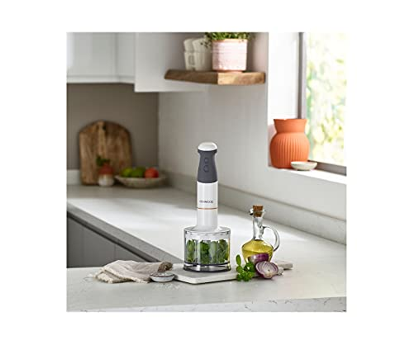 Blender ręczny ze składnikami na blacie. W tle okno i półki z roślinami.