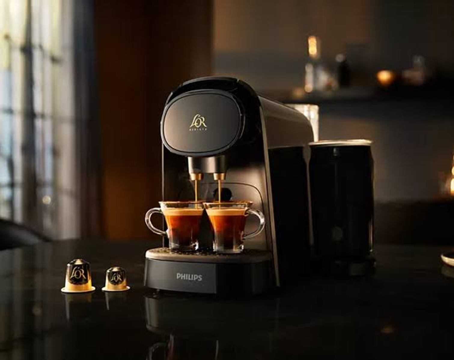 Una máquina de espresso negra con dos tazas de café vertiéndose. Dos cápsulas de café debajo.