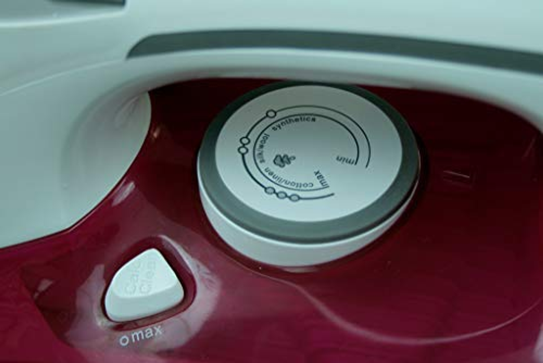 Primer plano del dial de temperatura de la plancha. Tiene ajustes para diferentes tejidos y color blanco.