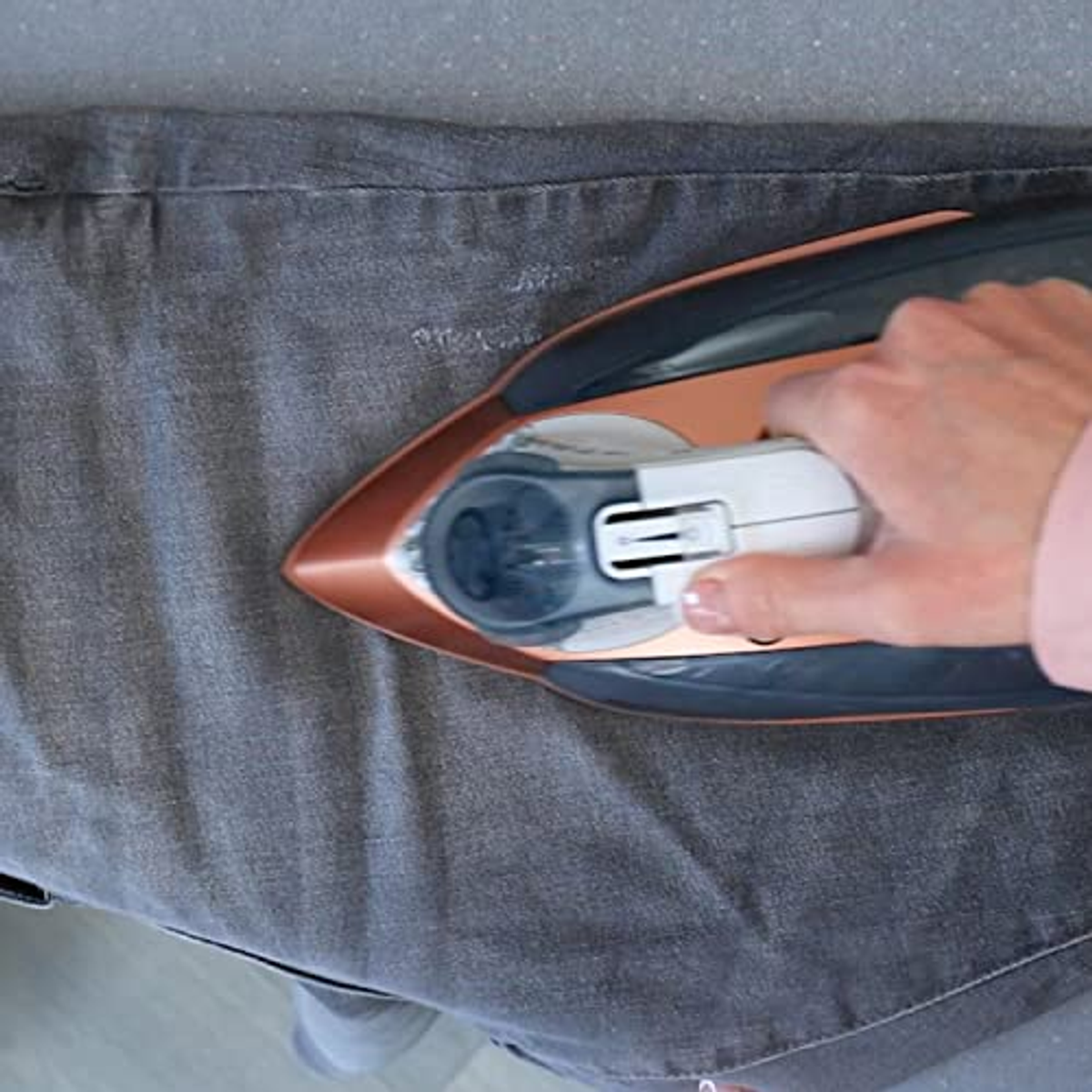 Eine Person bügelt eine graue Hose mit einem kupferfarbenen Bügeleisen.