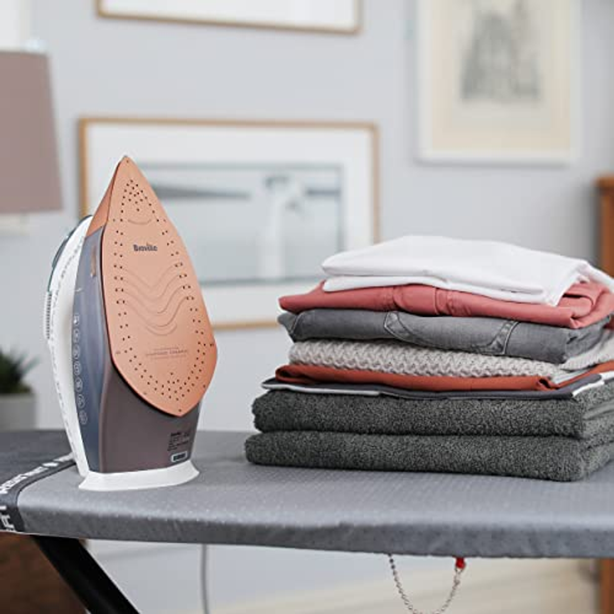 Bügeleisen auf Bügelbrett, mit gefalteter Kleidung. Bügeleisen ist braun und grau.