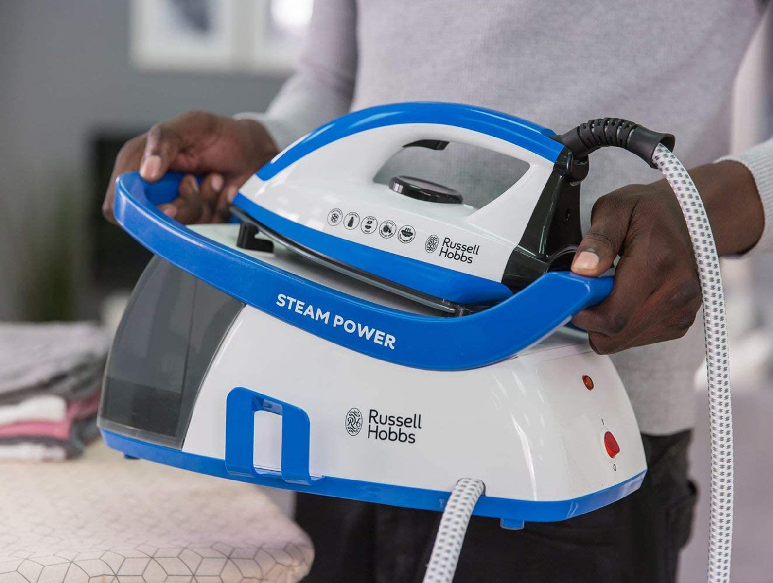 Una persona tiene in mano un ferro da stiro a vapore Russell Hobbs blu e bianco. Il ferro è su una base bianca.