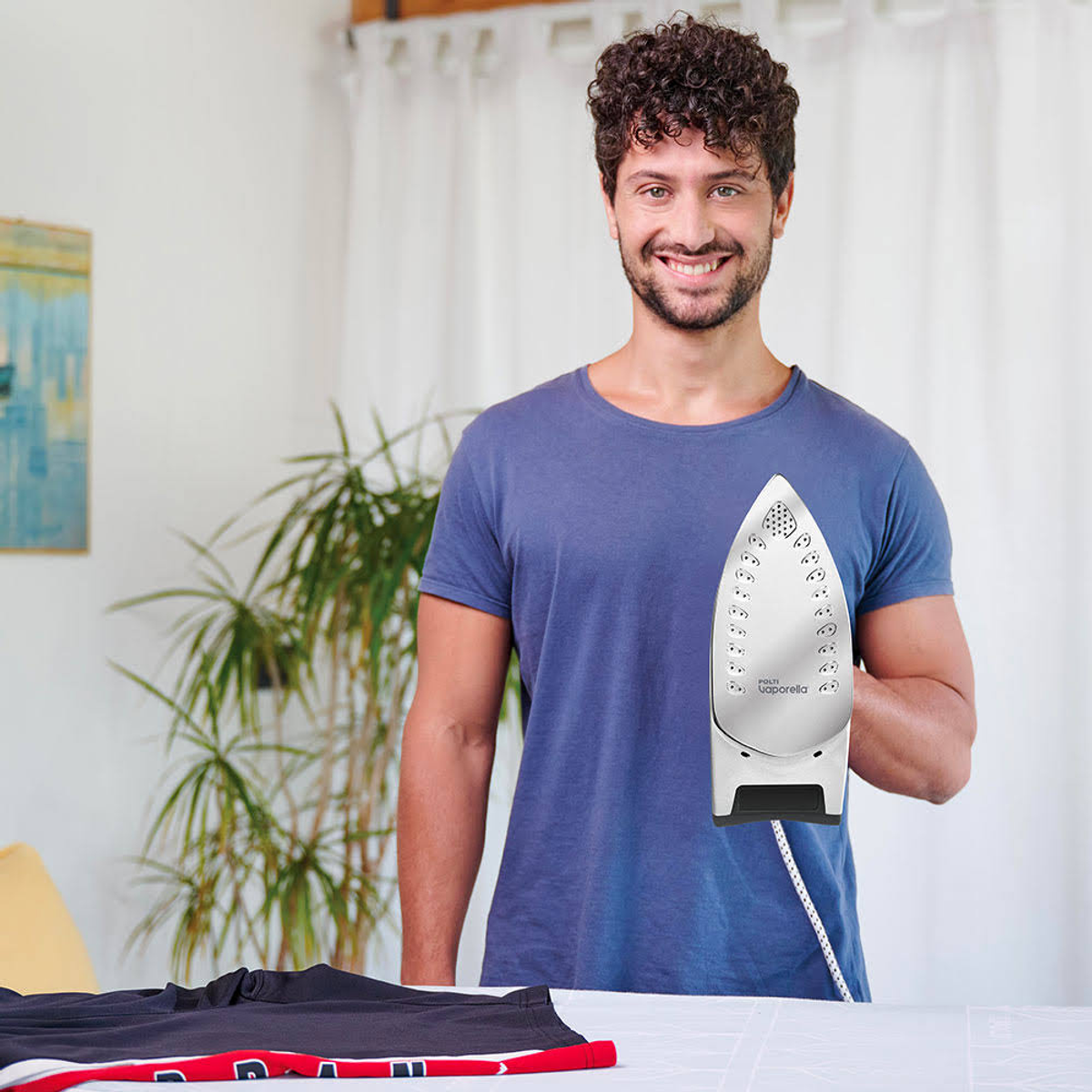 Mężczyzna trzymający żelazko, uśmiechnięty, z koszulą i praniem.