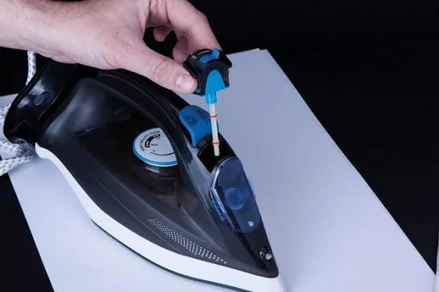 Mano llenando el depósito de agua de la plancha. Papel blanco detrás.