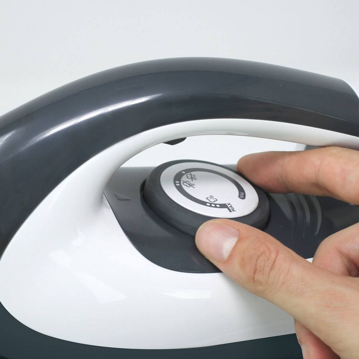 La mano di una persona che gira il quadrante di un ferro da stiro bianco e grigio. Sfondo bianco.