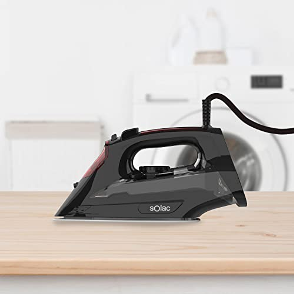 Plancha negra sobre una mesa de madera. Lavadora y secadora al fondo.