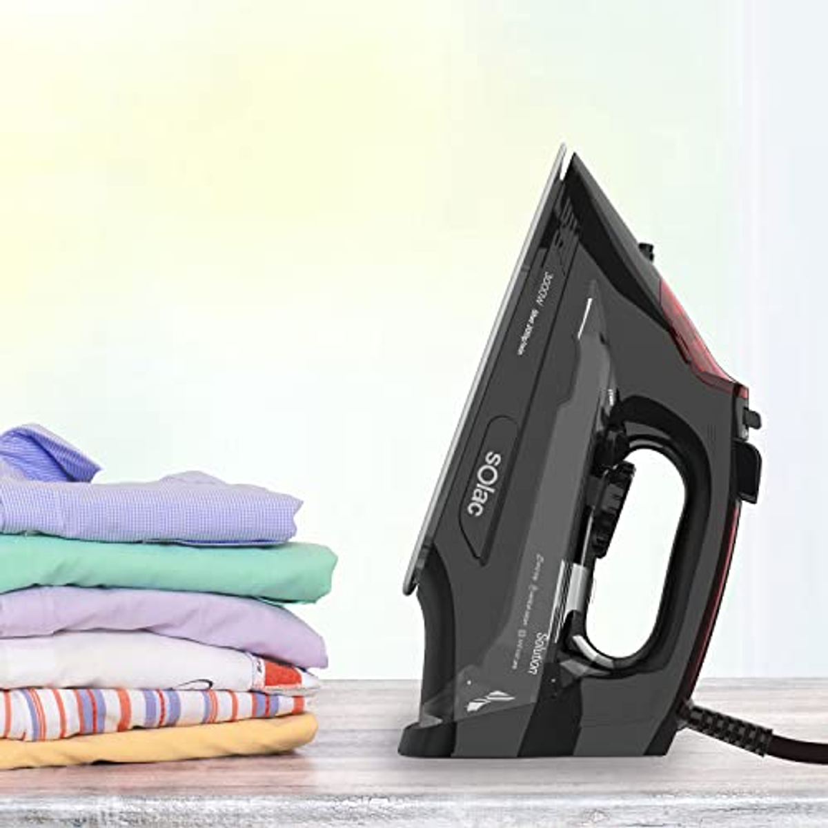 Plancha negra y pila de camisas dobladas de colores sobre mesa de madera.