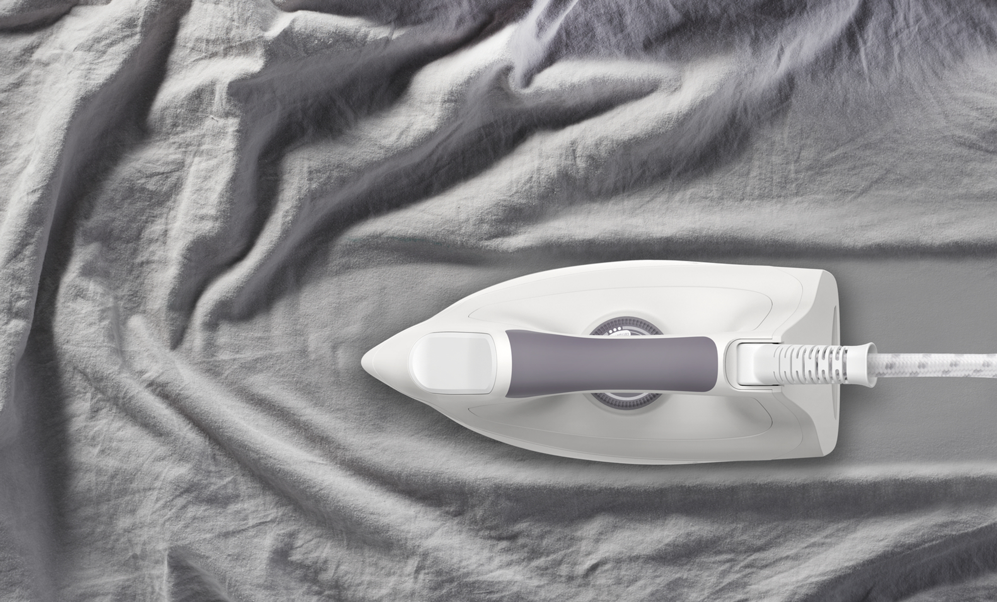 Una plancha sobre tela gris arrugada, con la plancha en la posición superior. La plancha es blanca y gris.