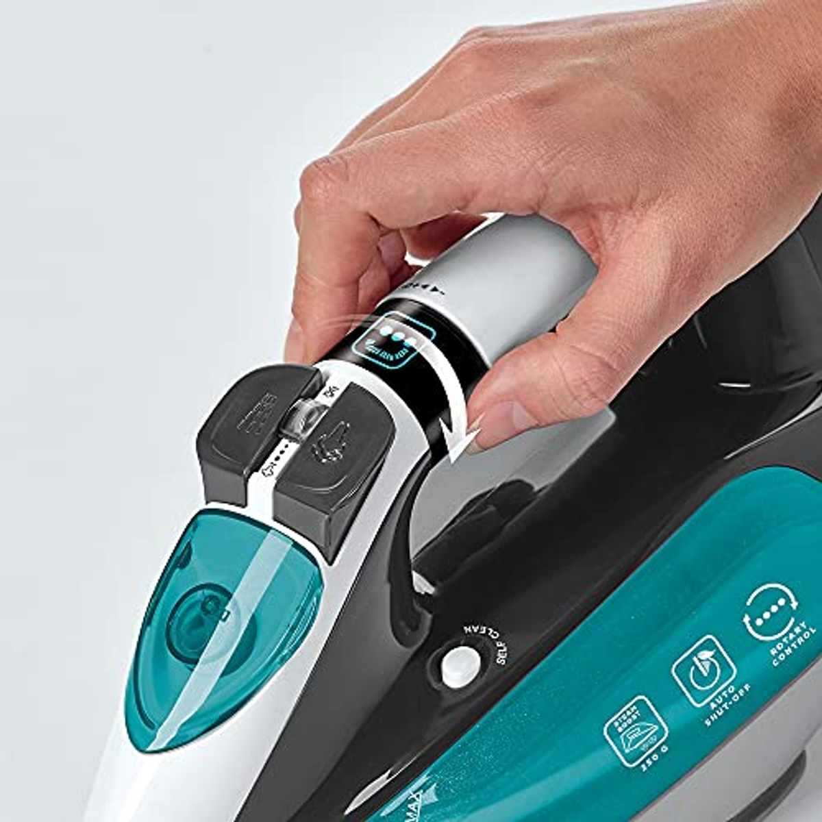 Ręka osoby regulująca pokrętło na czarnym i turkusowym żelazku. Żelazko znajduje się na białej powierzchni.