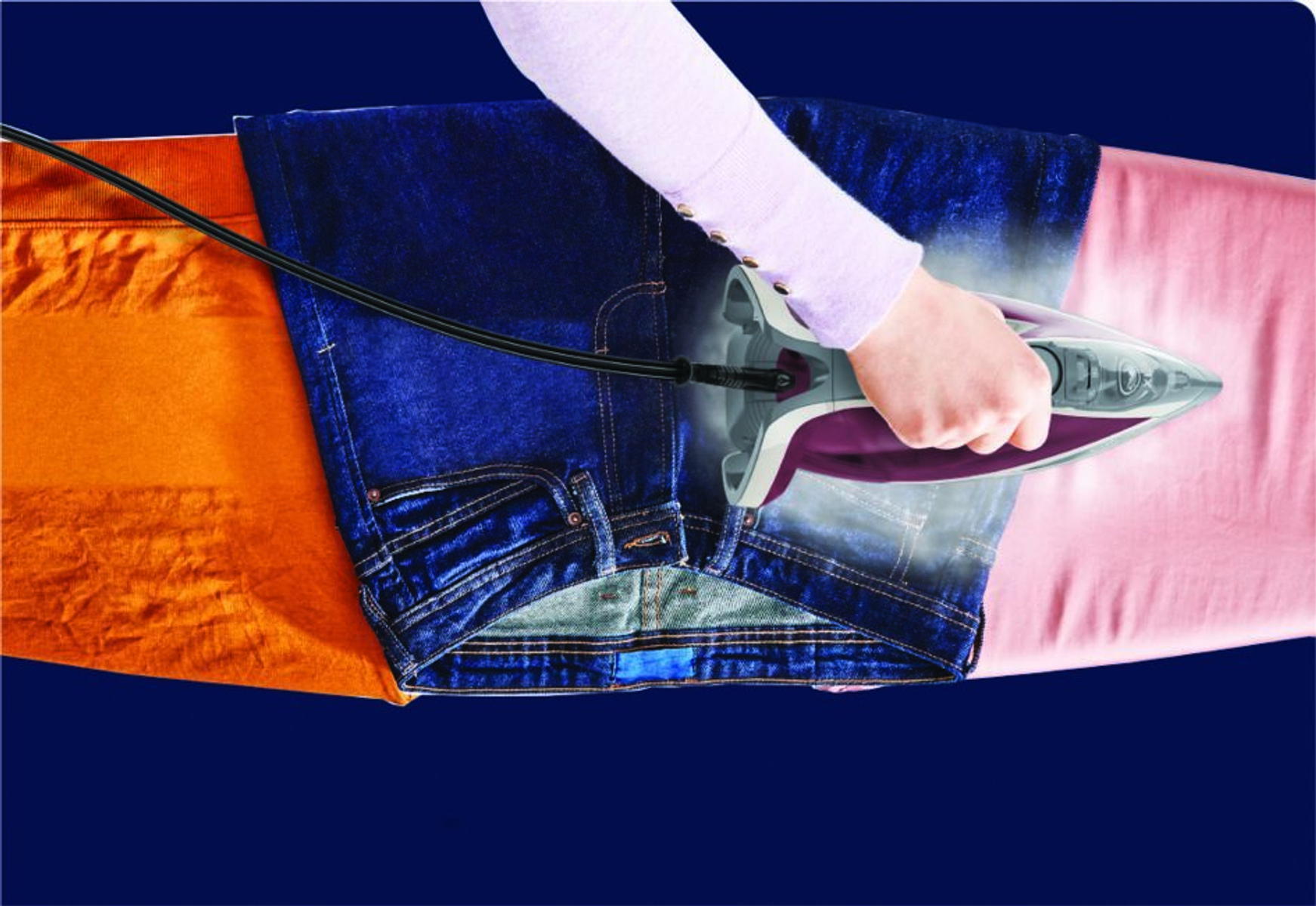 Eine Person bügelt blaue Jeans und orangefarbenen sowie rosa Stoff mit Dampf.