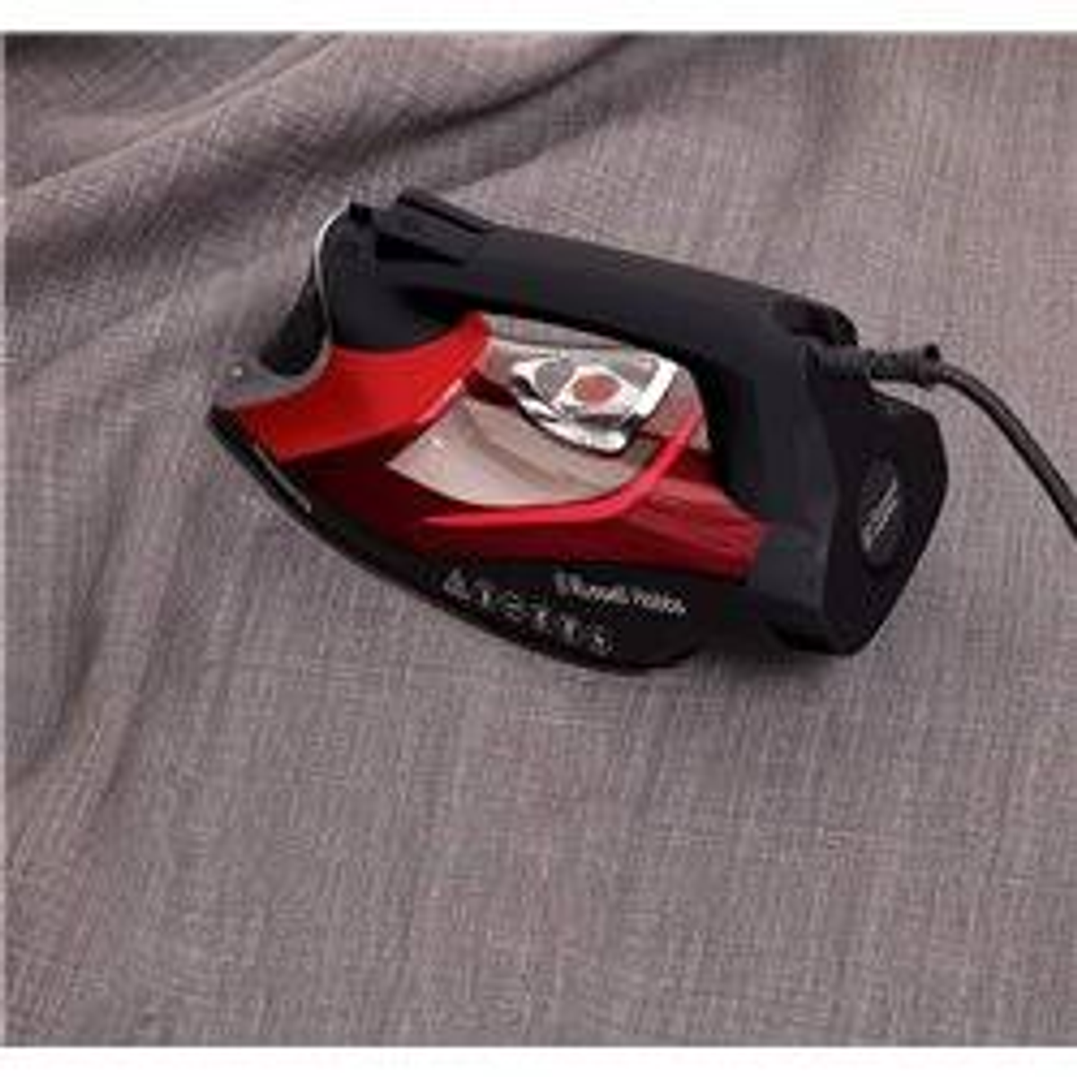 Czarne i czerwone żelazko na szarej tkaninie. Żelazko jest podłączone i ustawione pod kątem.