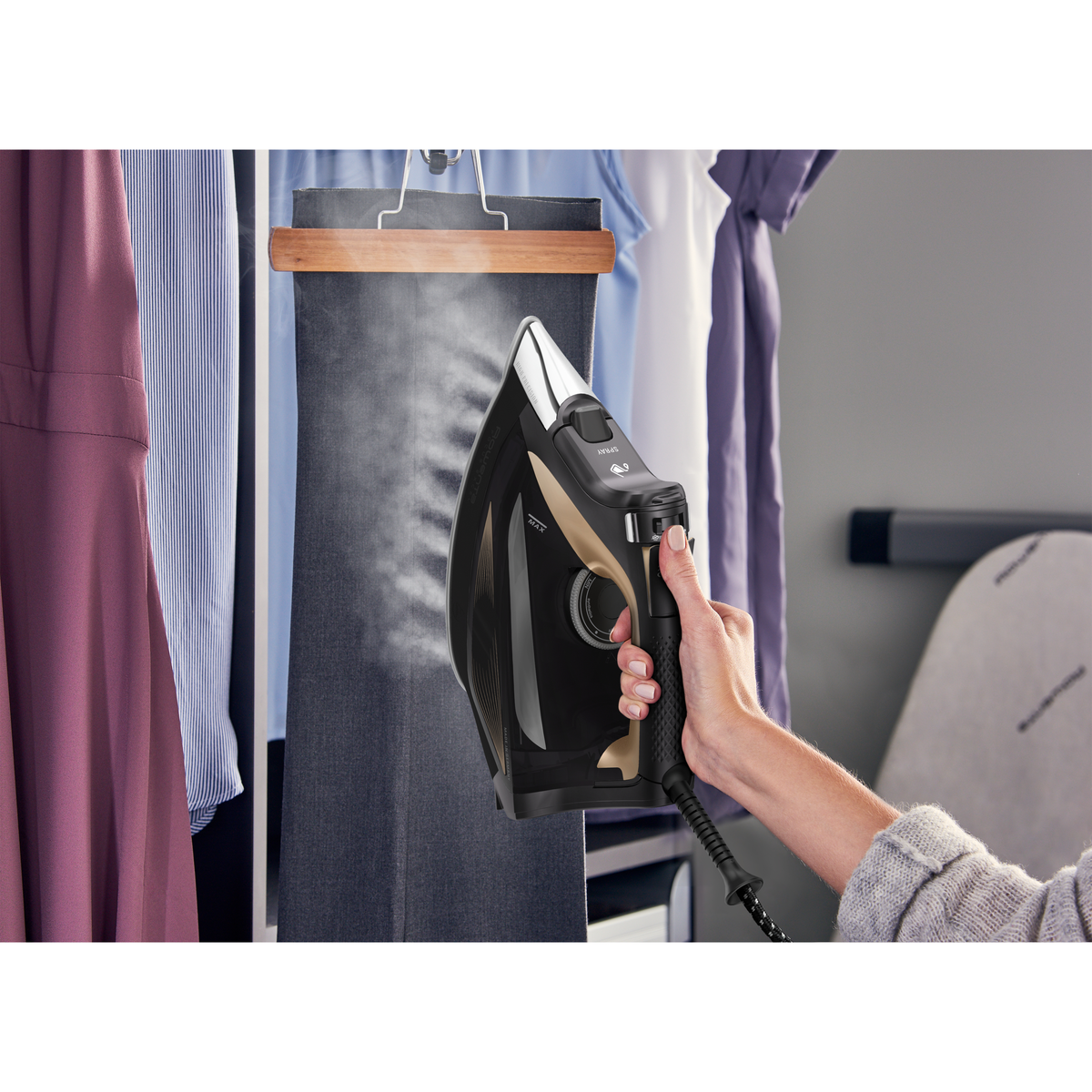 Stiratura a mano di un pantalone scuro su un appendiabiti. Il ferro è nero e oro.