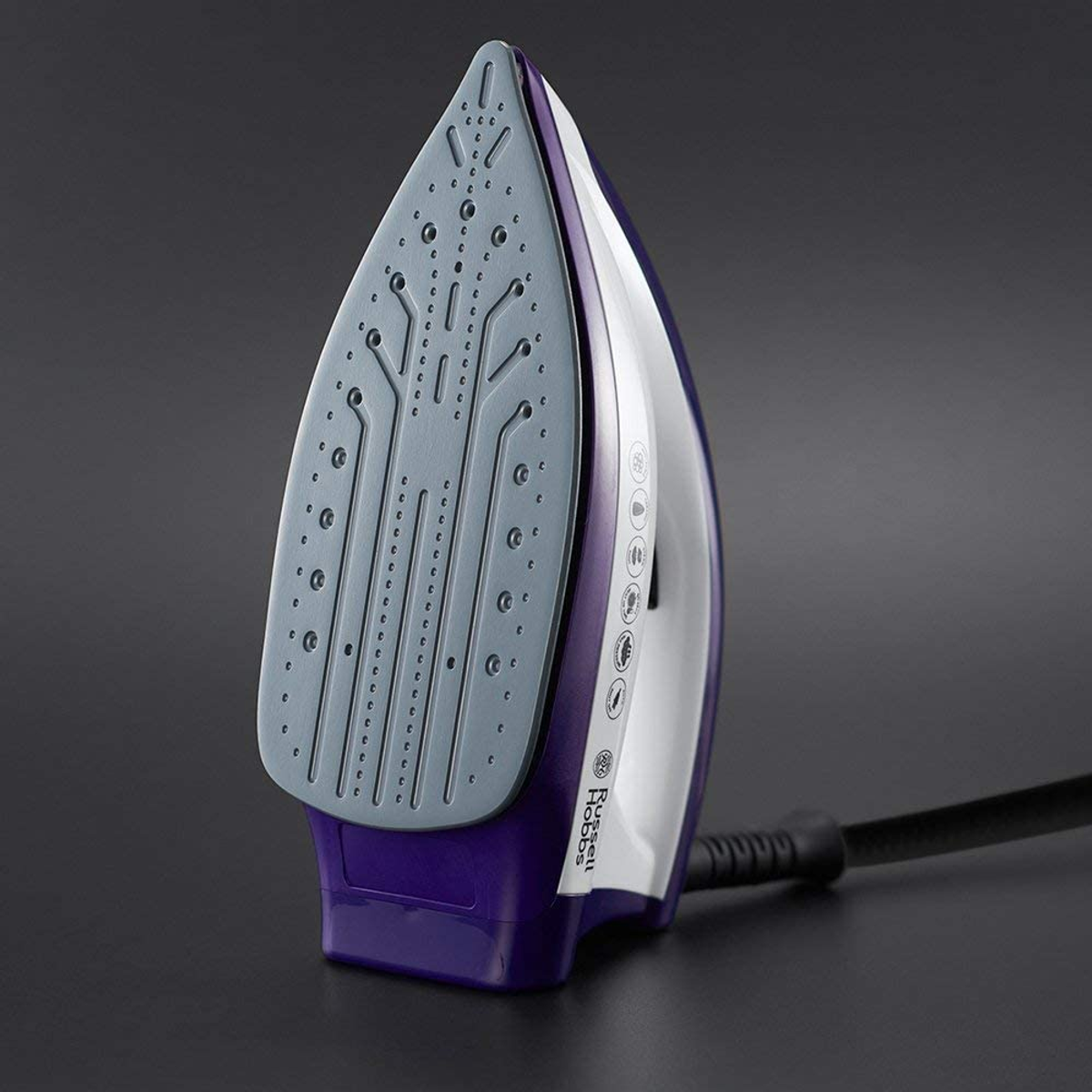 Plancha morada y blanca sobre una superficie oscura. La plancha tiene suela gris y cable negro.