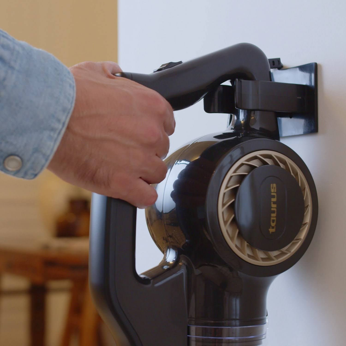 Ręka trzymająca odkurzacz bezprzewodowy. Czarno-złoty design, zamontowany na ścianie.