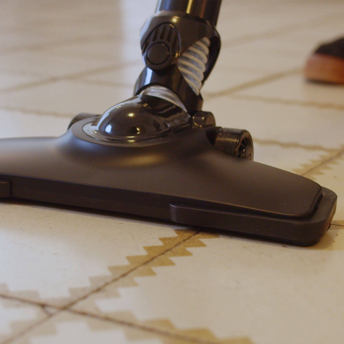 Czarna głowica odkurzacza na podłodze z wzorzystych płytek. Podłoga jest jasna.