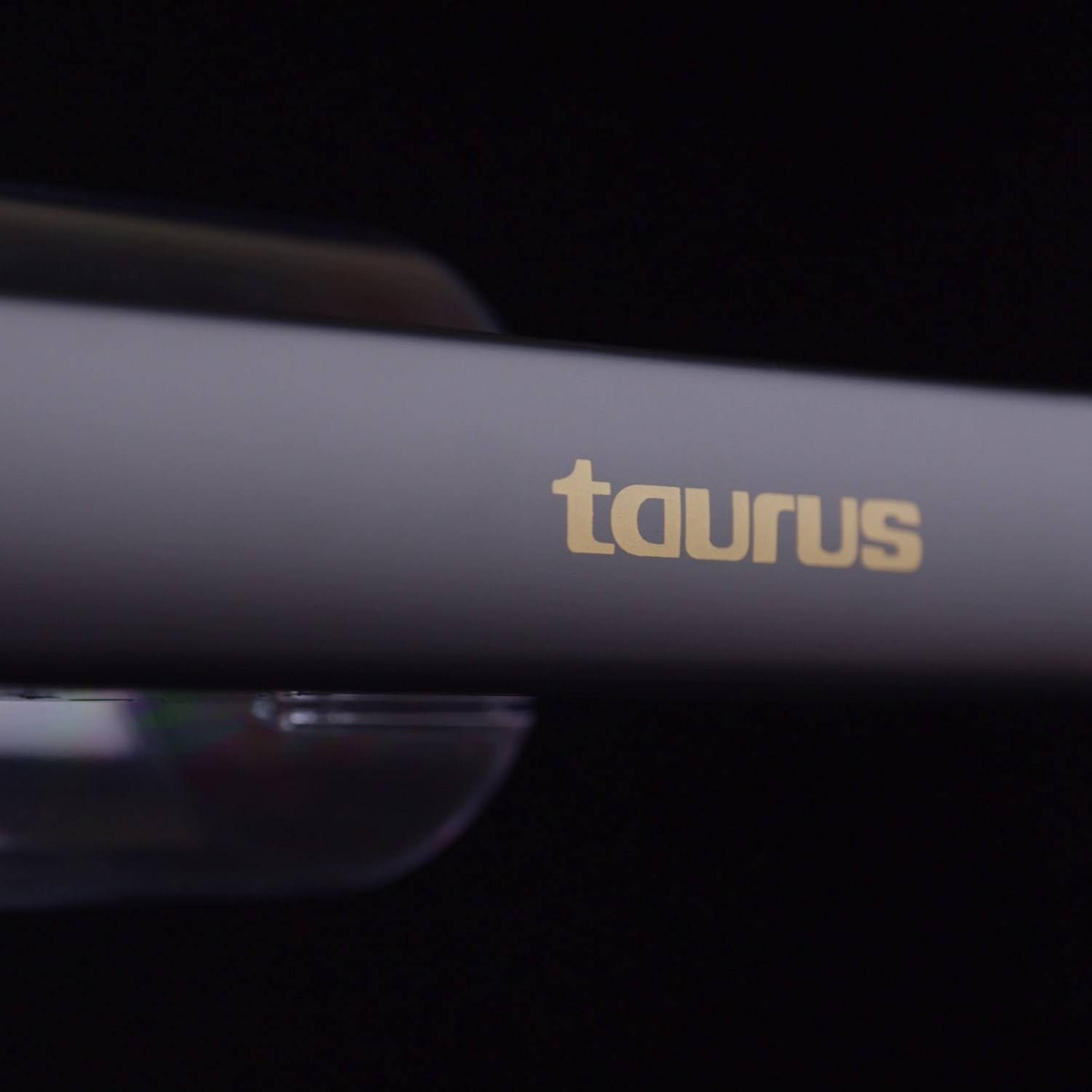 Zbliżenie szarej prostownicy Taurus ze złotym logo 'taurus' na czarnym tle.