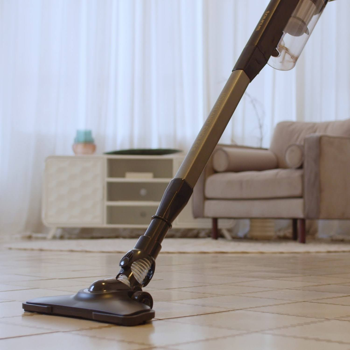 Odkurzacz czyszczący podłogę z płytek. Sofa i stolik w tle. Jasne, przestronne otoczenie.