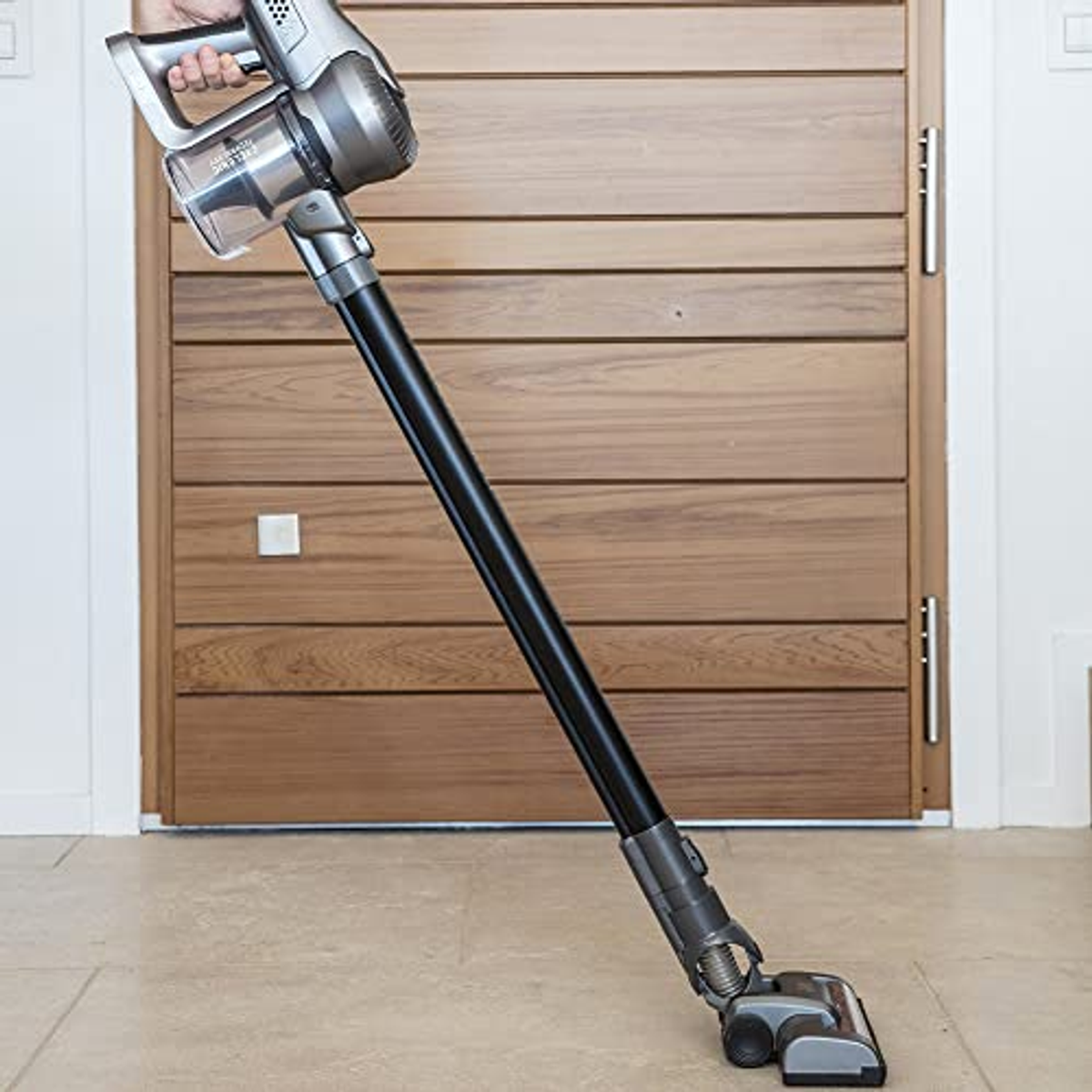 Eine Person benutzt einen silbernen, kabellosen Staubsauger auf einem Holzboden.