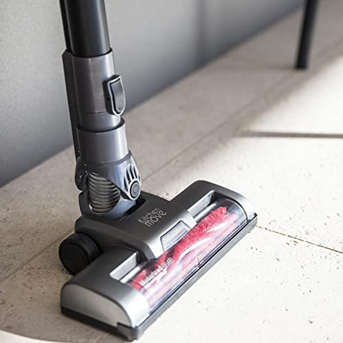 Nahaufnahme eines grauen Staubsaugerkopfes mit roter Bürste auf hellem Fliesenboden.