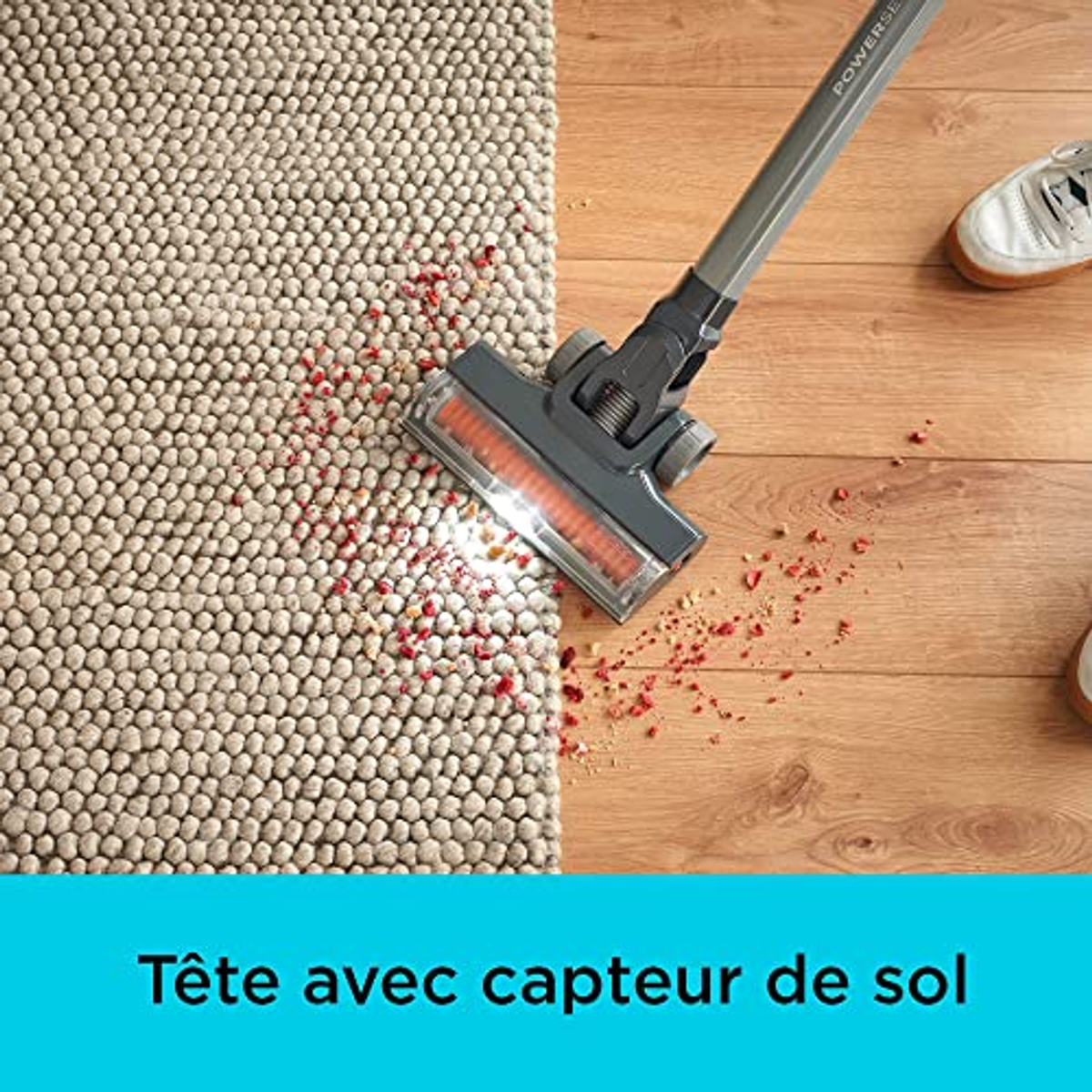Un aspirapolvere che pulisce un tappeto. C'è una macchia rossa sul tappeto. Il pavimento è in legno.