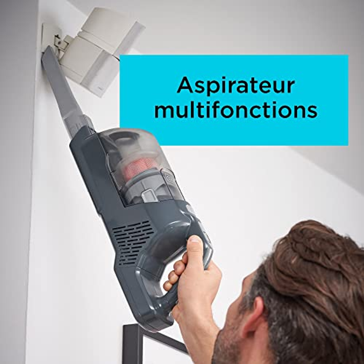 Uomo che tiene un aspirapolvere portatile grigio, testo: Aspirateur multifonctions, su scatola blu.