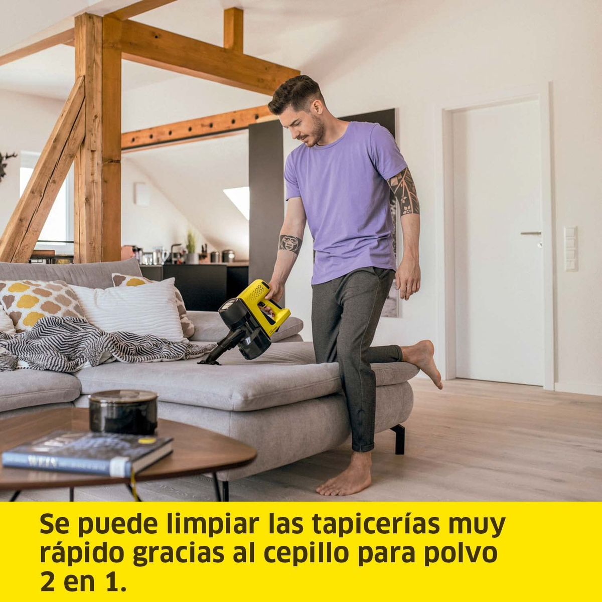 Uomo che passa l'aspirapolvere su un divano grigio con un aspirapolvere portatile giallo. Interno della stanza.