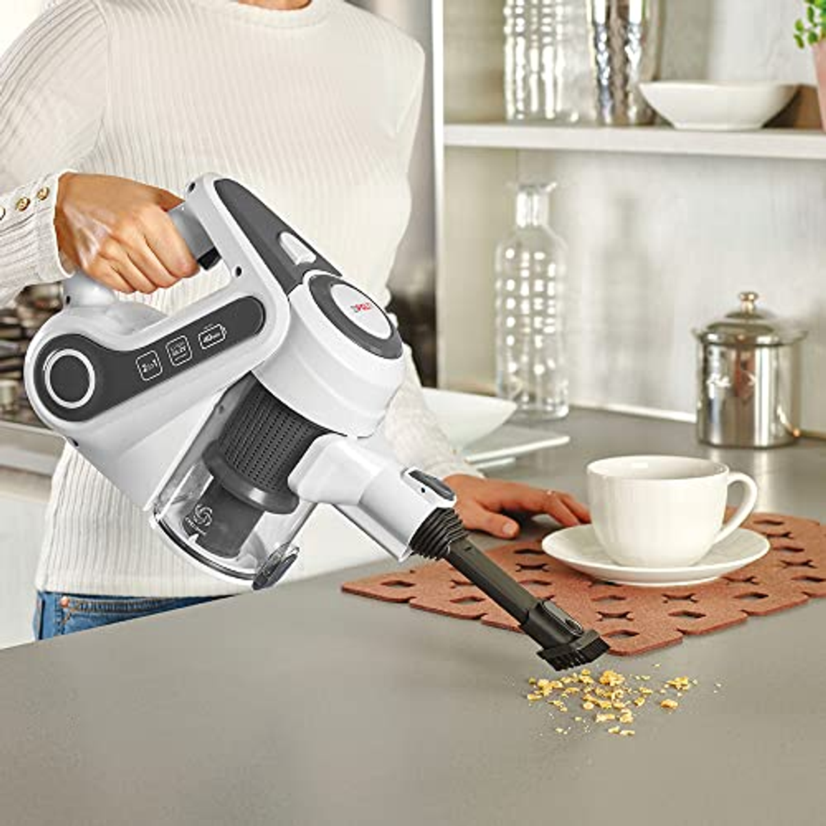 Eine Person benutzt einen weiß-grauen Staubsauger auf einer Theke.