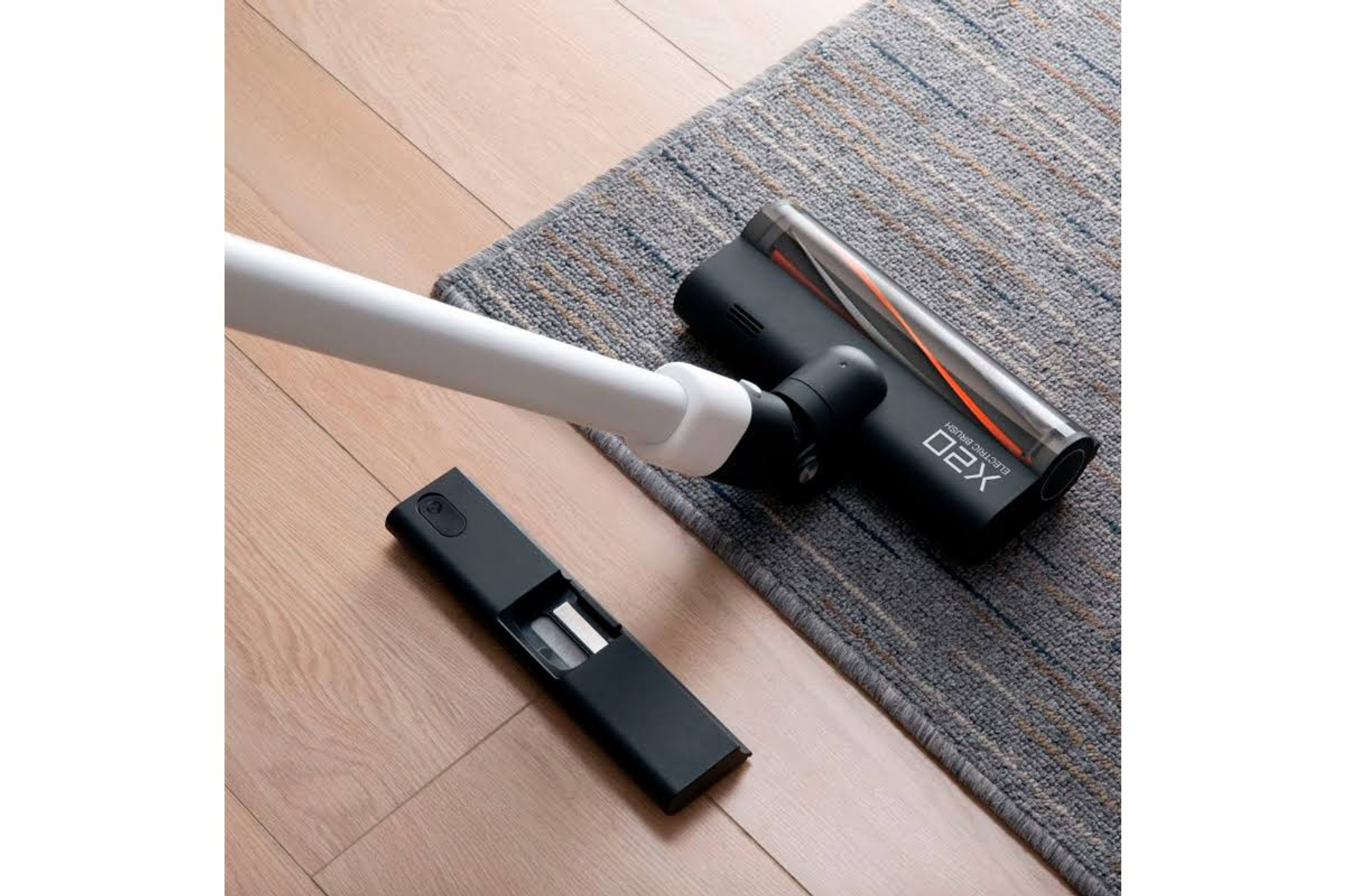 Aspirapolvere con accessori su pavimento in legno e un tappeto.