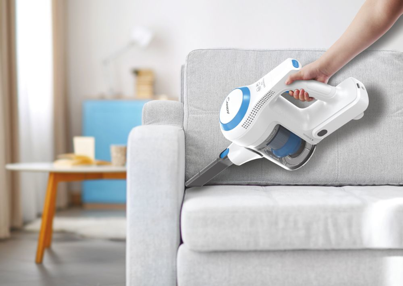 Hand benutzt einen weiß-blauen Staubsauger auf einem grauen Sofa. Weißer Hintergrund.