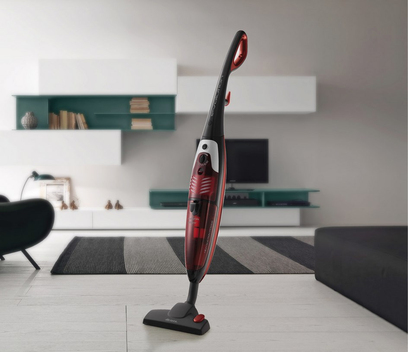Czerwono-czarny odkurzacz w salonie. Stoi wyprostowany.