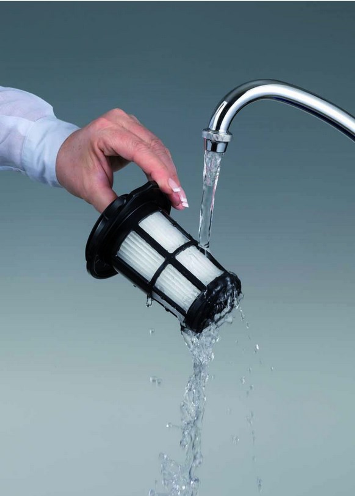 Ręka myje filtr odkurzacza pod kranem.