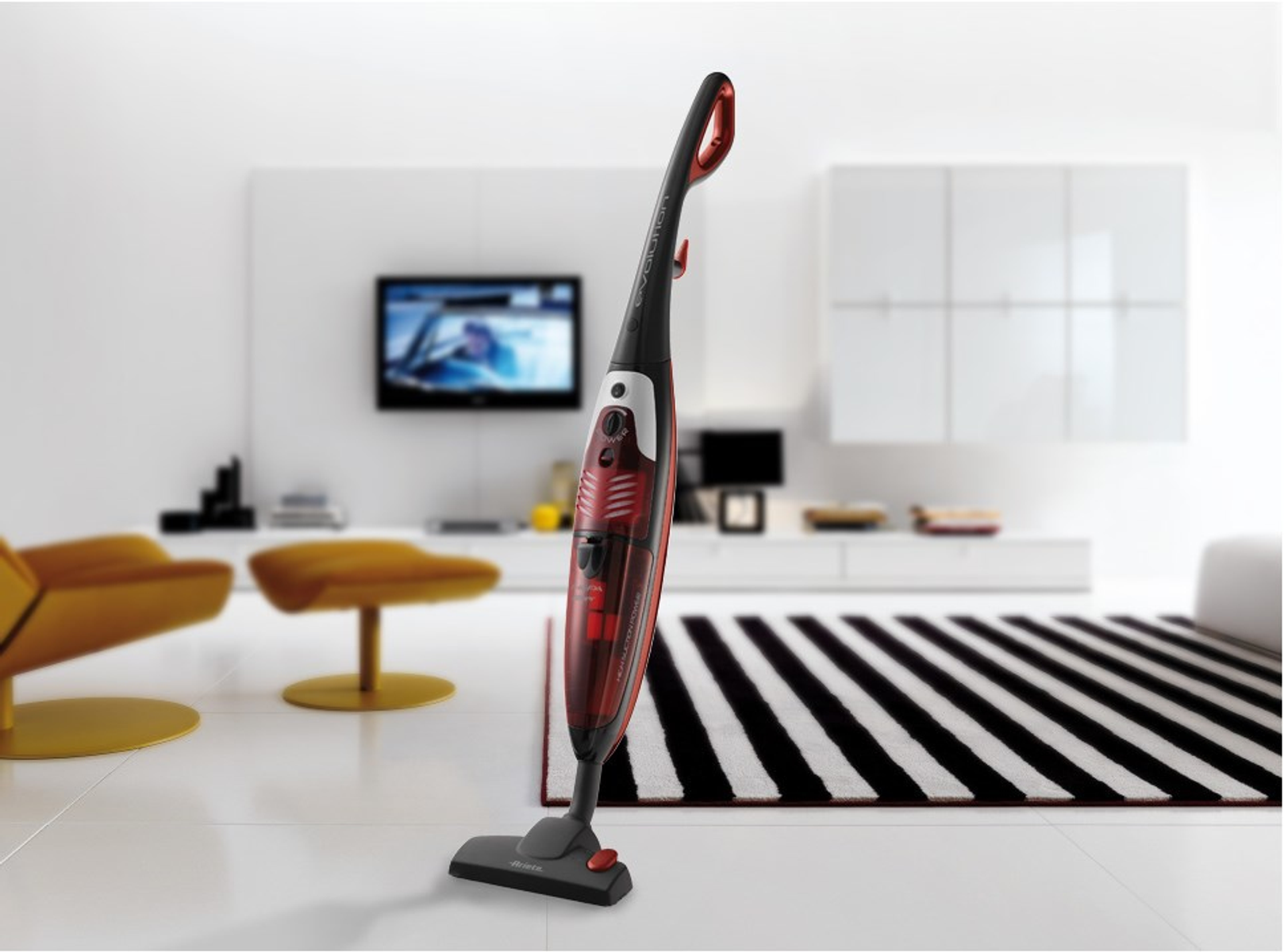 Czerwono-czarny odkurzacz na białej podłodze, przed nowoczesnym salonem.