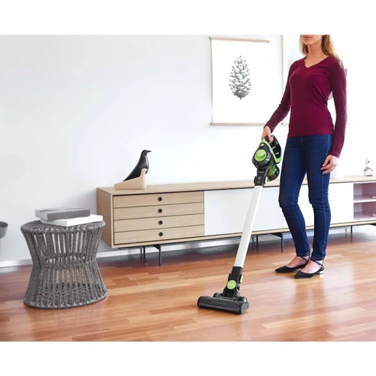 Mujer usando una aspiradora inalámbrica blanca y verde en un piso de madera.