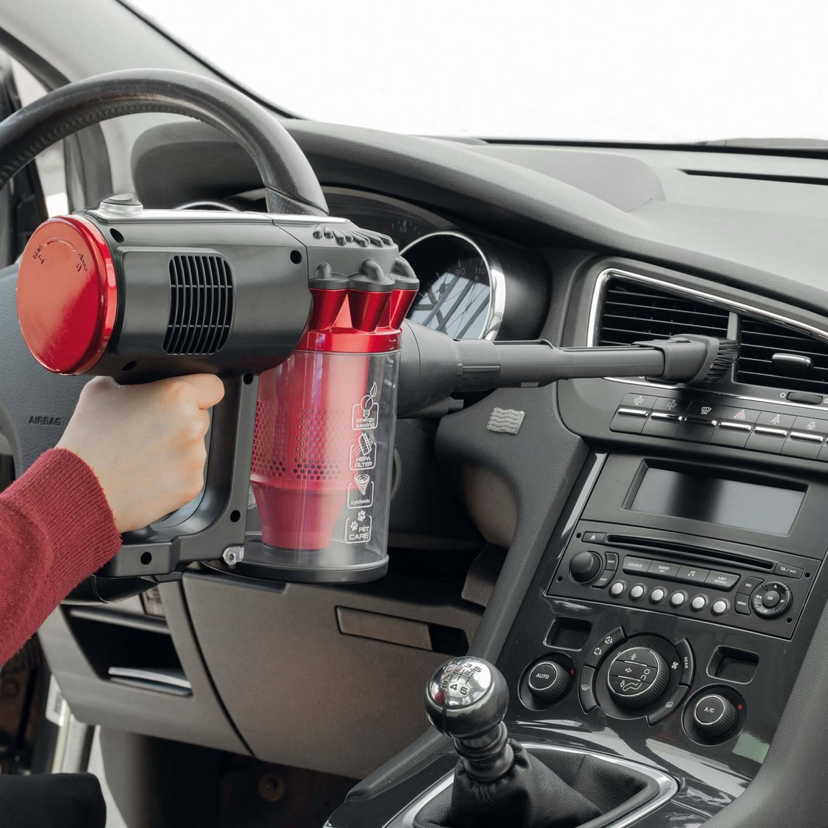Die Hand einer Person, die einen rot-schwarzen Handstaubsauger in einem Auto hält.
