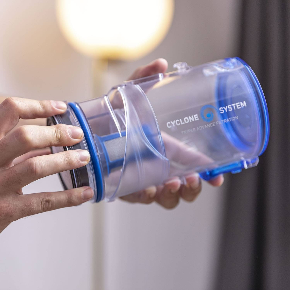 Eine Person hält einen transparenten Zylinder mit blauem Ring. Der Zylinder trägt die Aufschrift "Cyclone System".