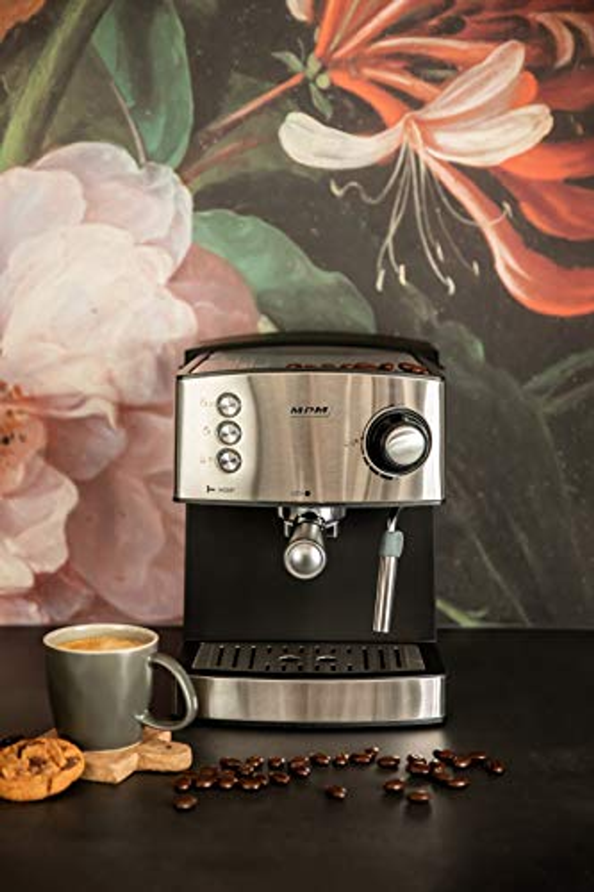 Máquina de espresso con taza y galletas. Granos de café esparcidos sobre la superficie negra, fondo floral.