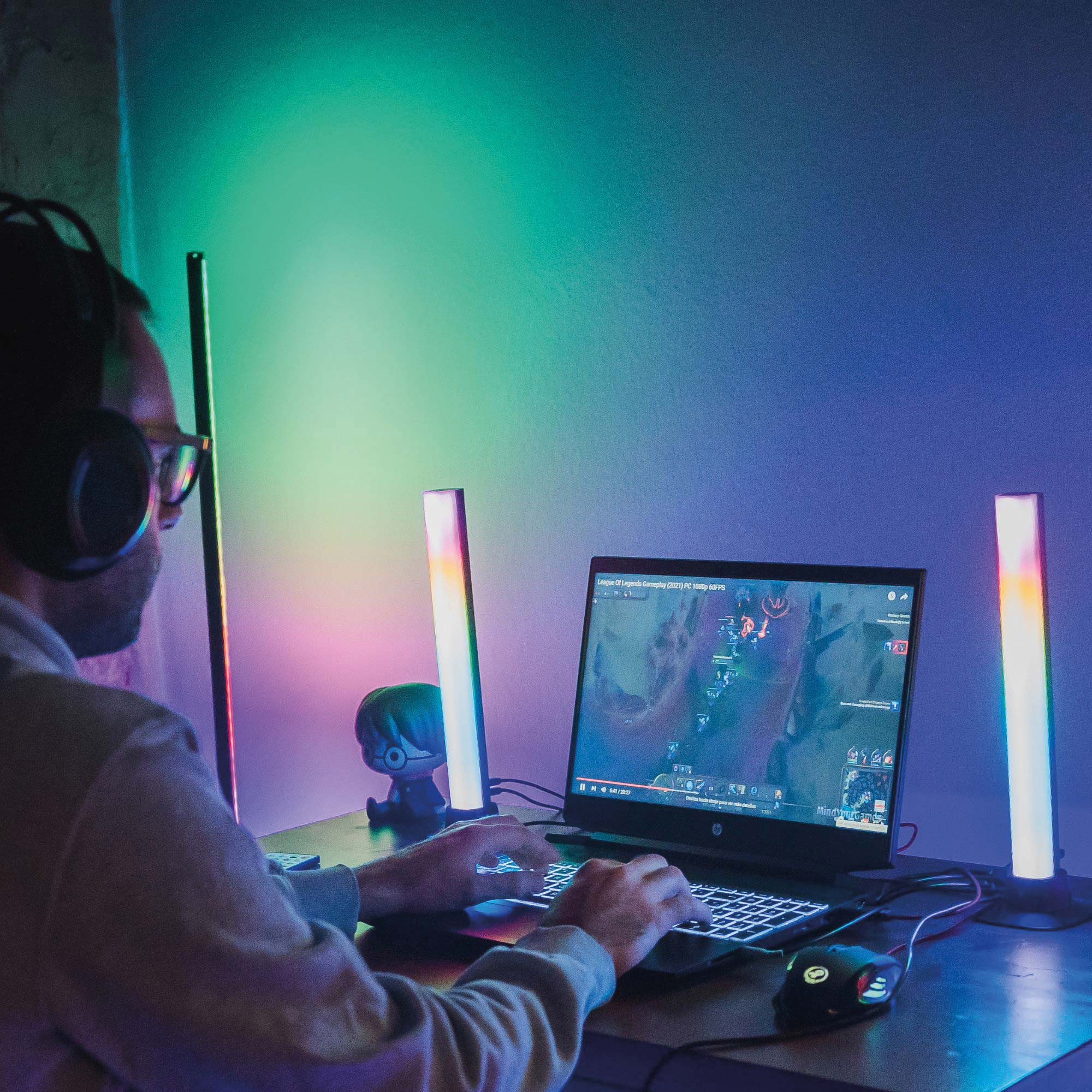 Osoba gra. Na biurku znajdują się dwie kolorowe lampki LED i laptop.