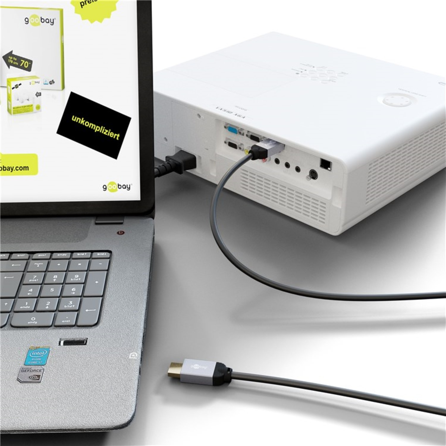 Ein Laptop, der mit einem weißen Projektor verbunden ist, ein Kabel und ein Schild mit dem Wort 'unkompliziert'.