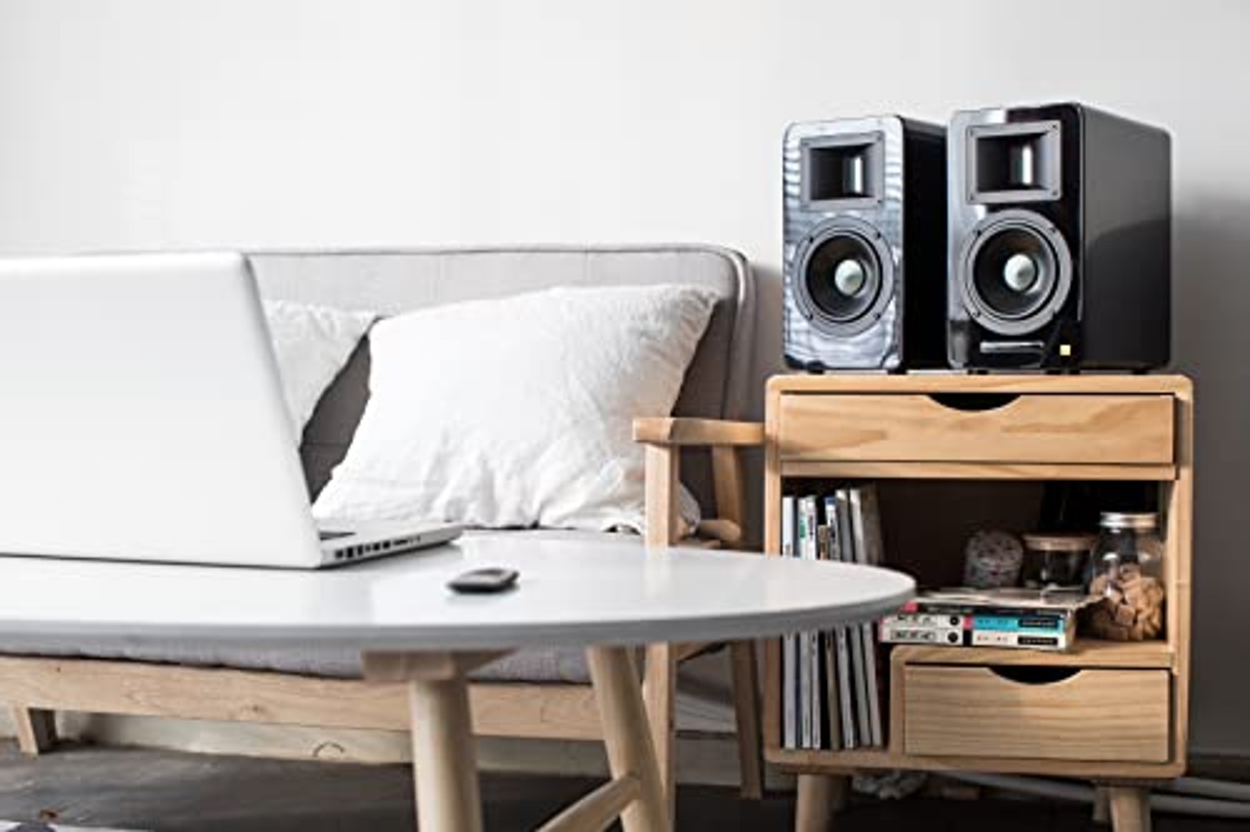 Laptop i głośniki na stole. Biała poduszka na sofie w tle.