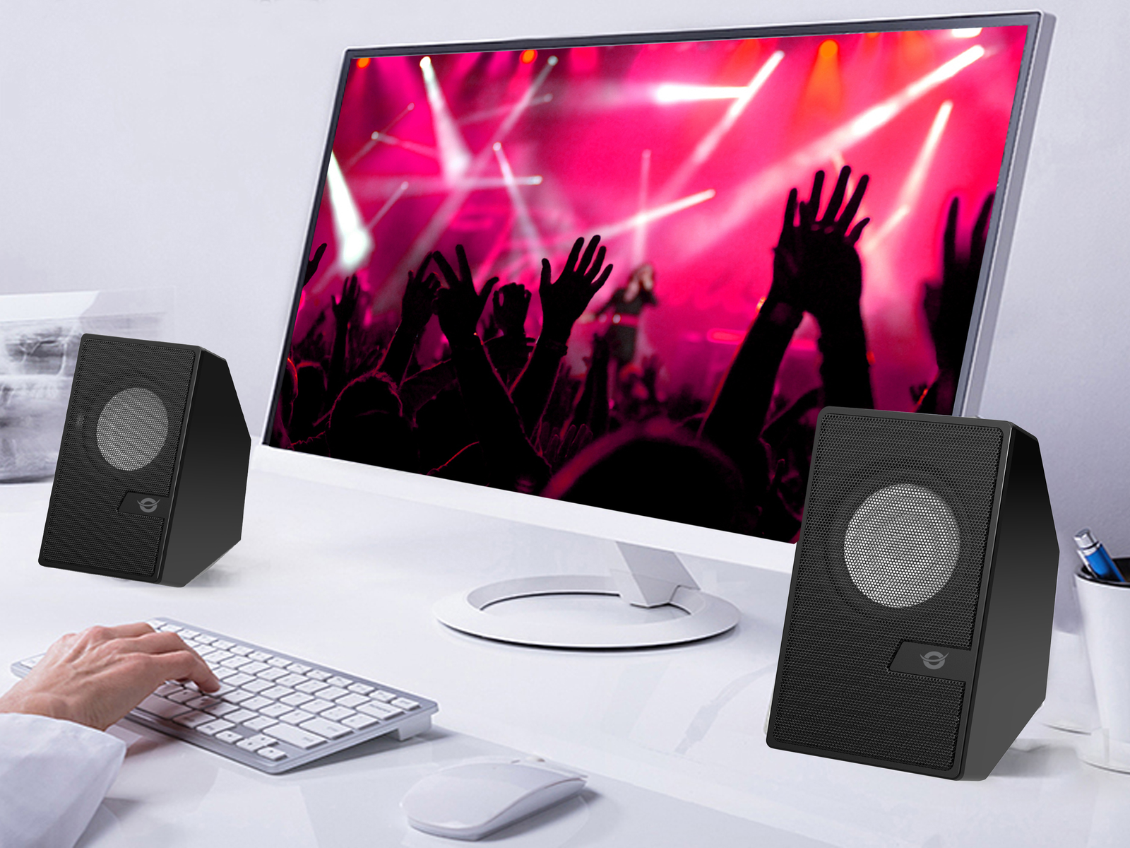 Due altoparlanti neri su una scrivania, un monitor mostra un concerto. Tastiera e mouse visibili.