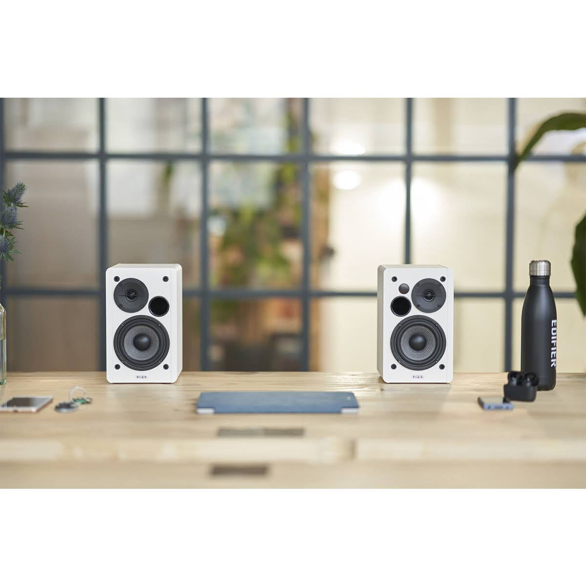 Dwa białe głośniki na drewnianym stole, z butelką i innymi przedmiotami.