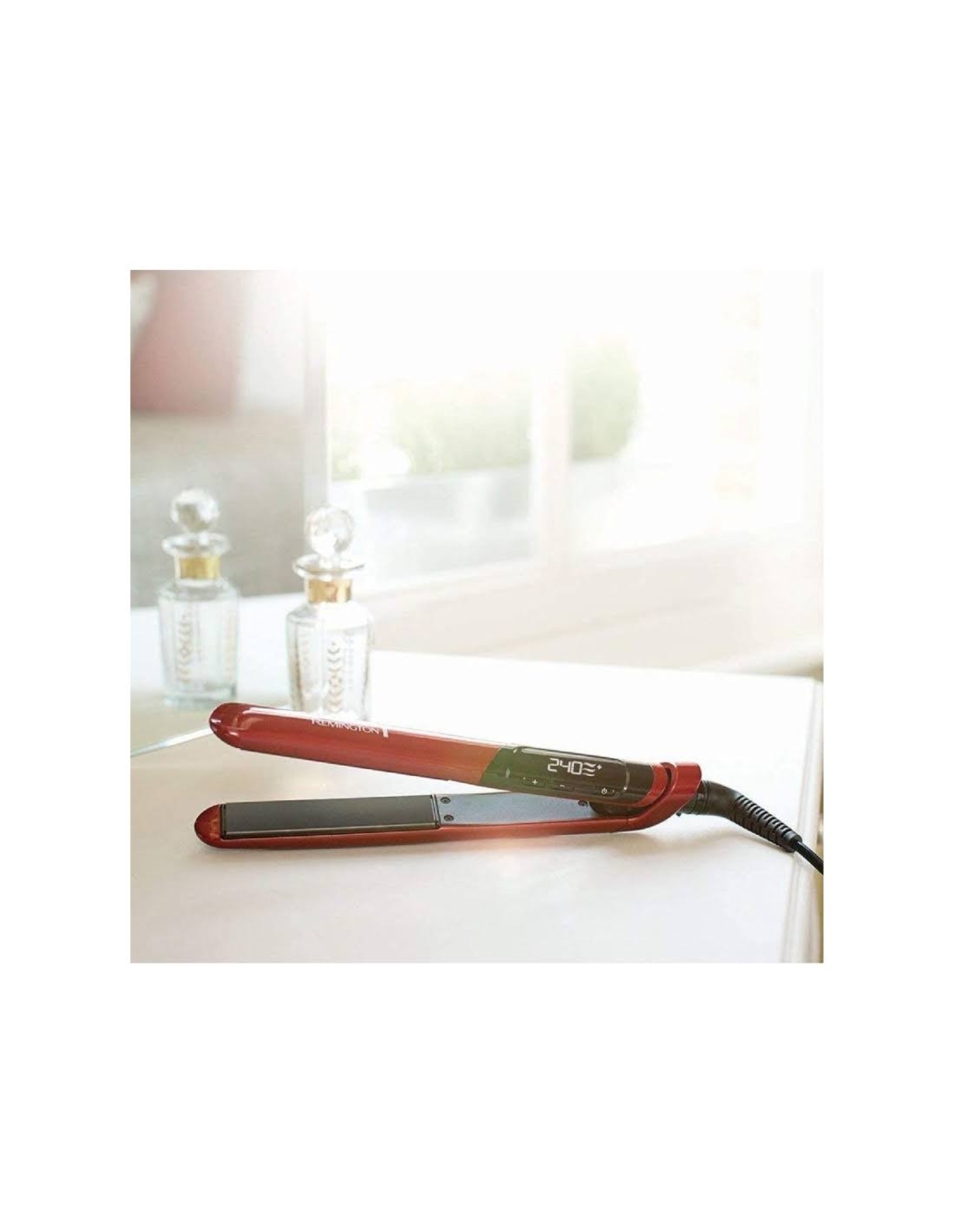Czerwona prostownica do włosów z wyświetlaczem cyfrowym, na białej powierzchni obok butelek.