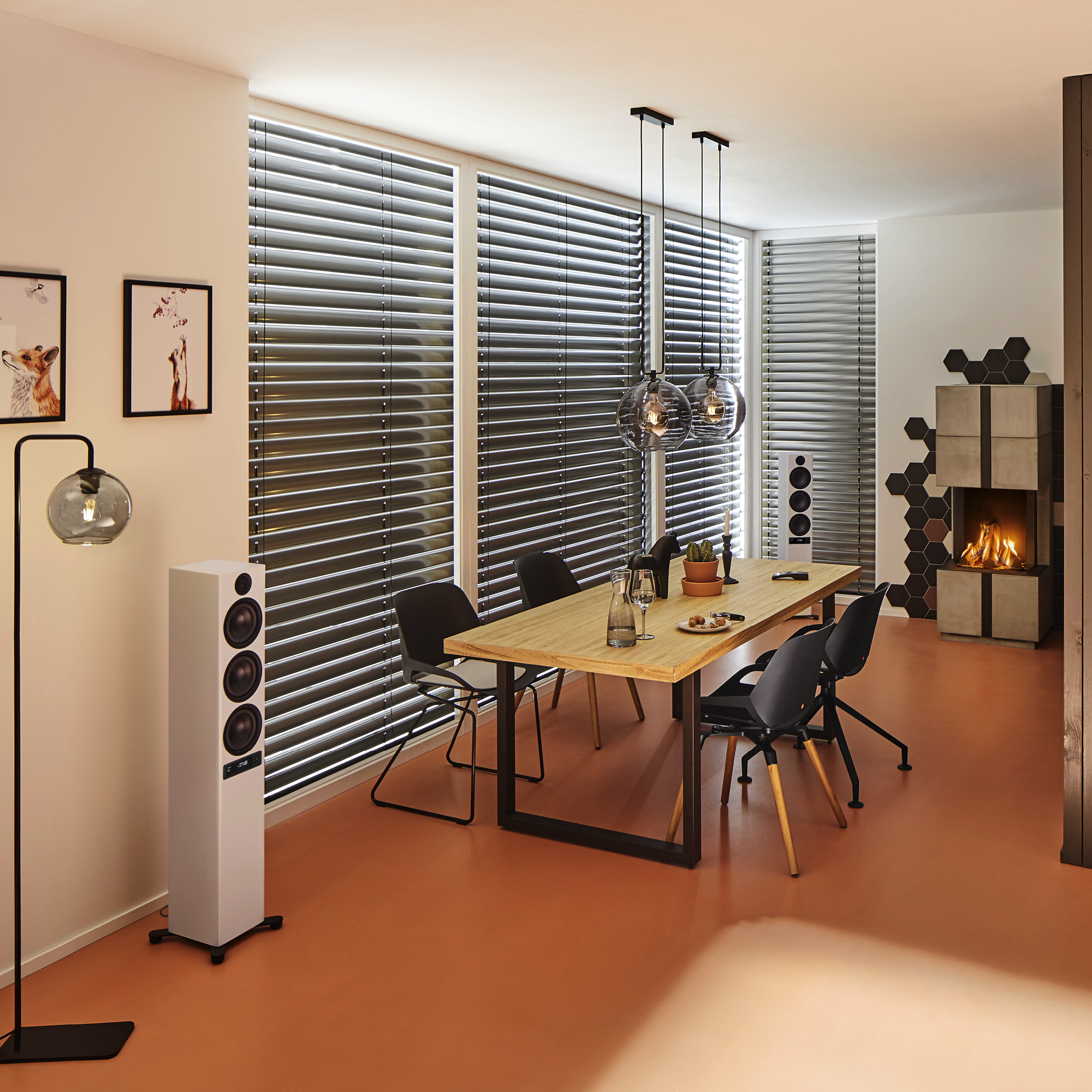 Ein Esszimmer mit Holztisch, schwarzen Stühlen, Kamin und hohem weißen Lautsprecher auf orangefarbenem Boden.