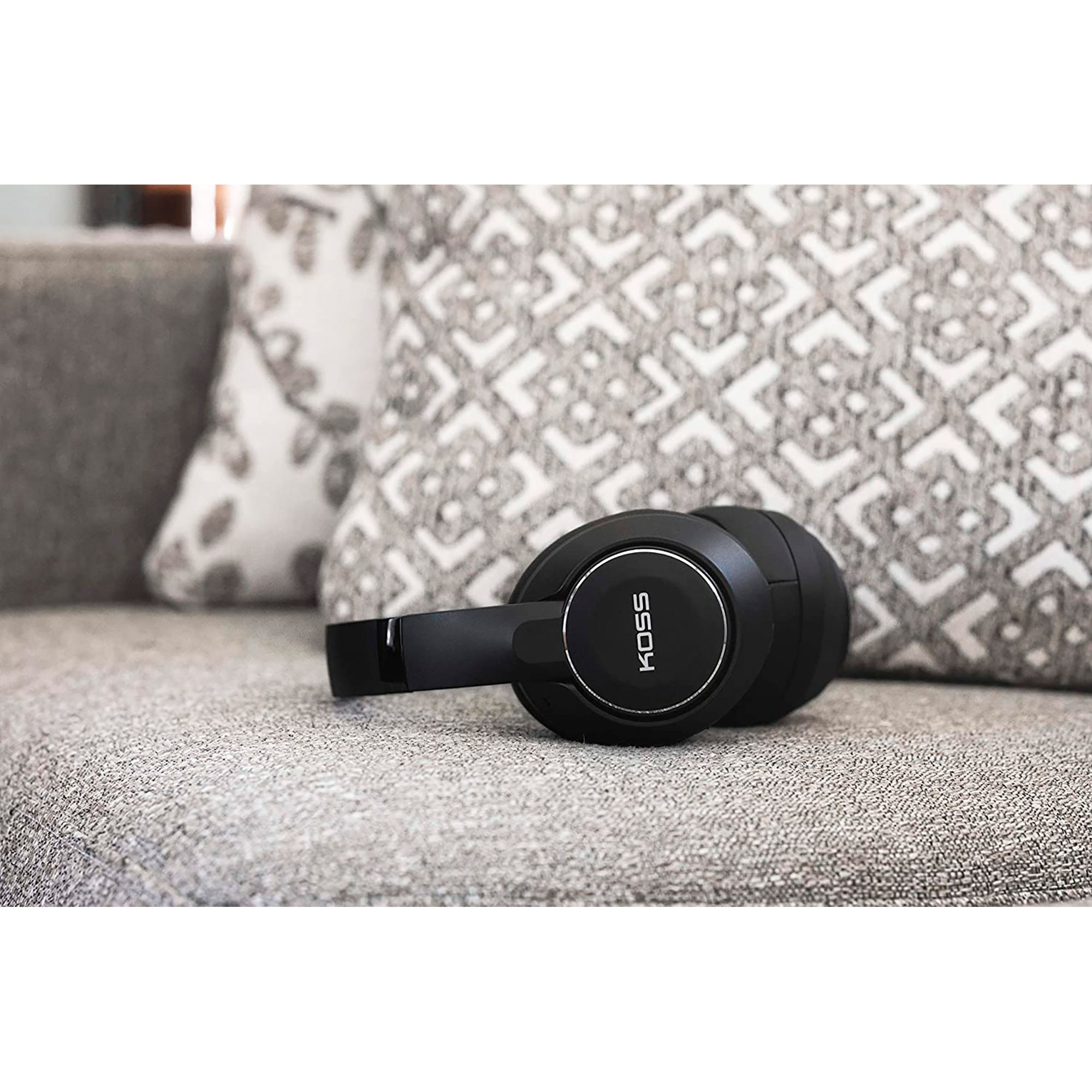 Casque noir posé sur un canapé gris, avec des coussins en arrière-plan.