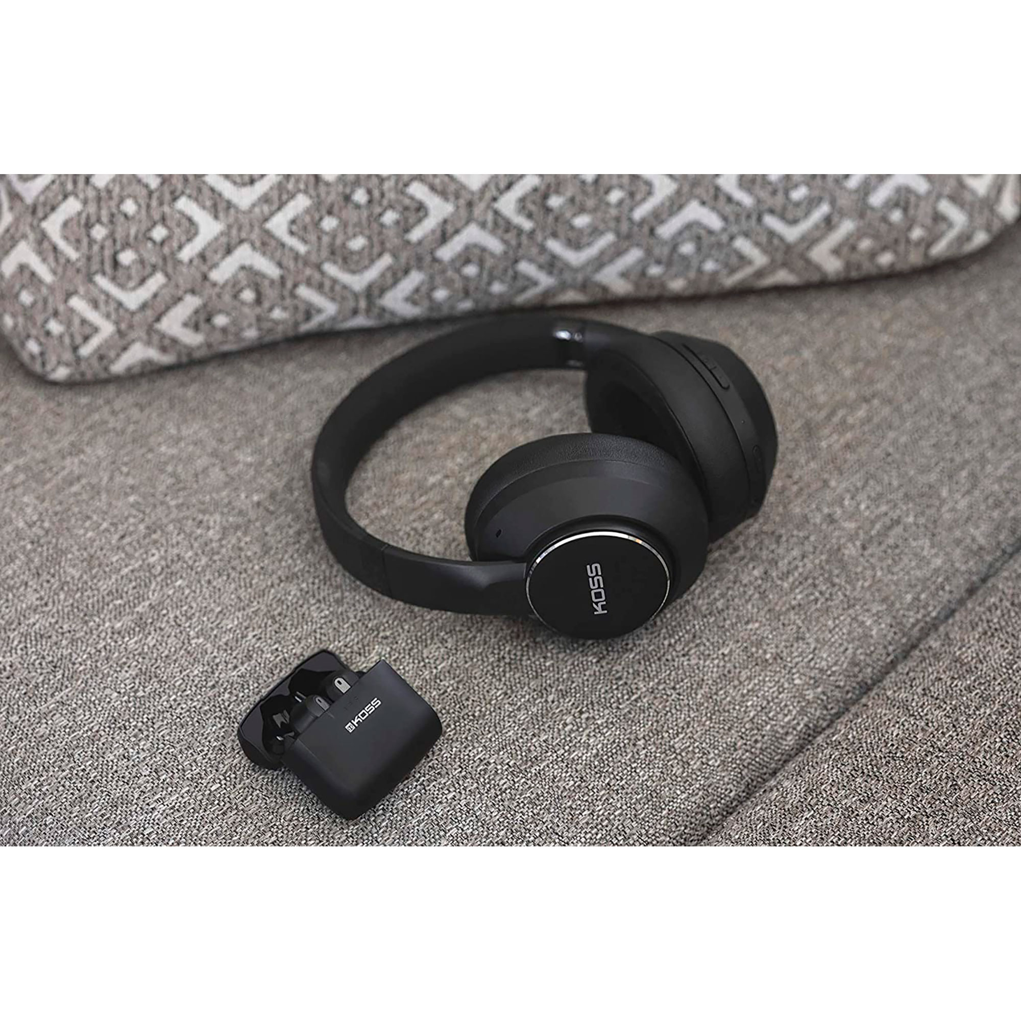 Casque et étui de chargement noirs sur un canapé gris. Le casque affiche la marque Koss.