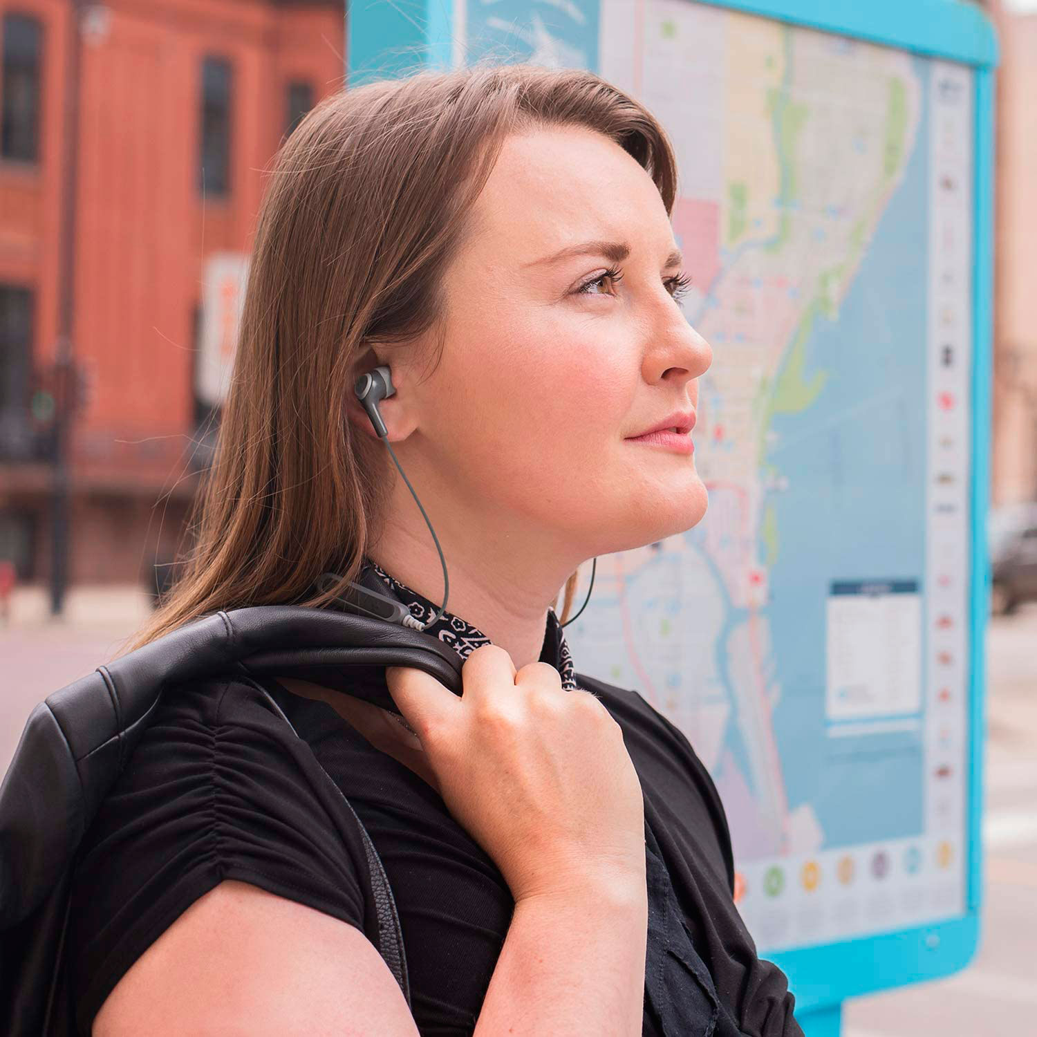 Donna con auricolari, guarda in alto. Tiene una giacca. Sfondo urbano con mappa.