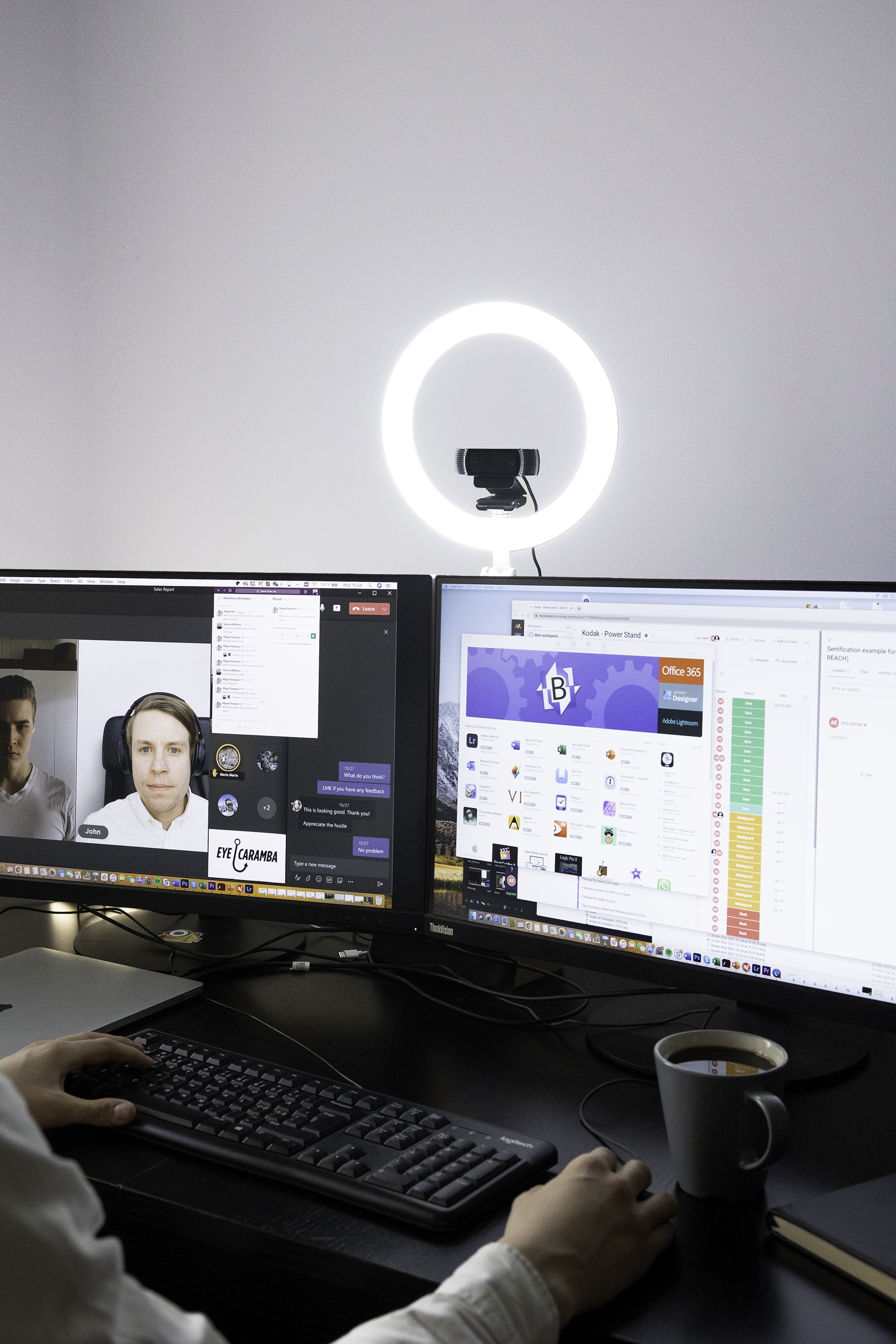 Eine Person arbeitet an einem Computer mit zwei Monitoren, Ringlicht und Kaffee.