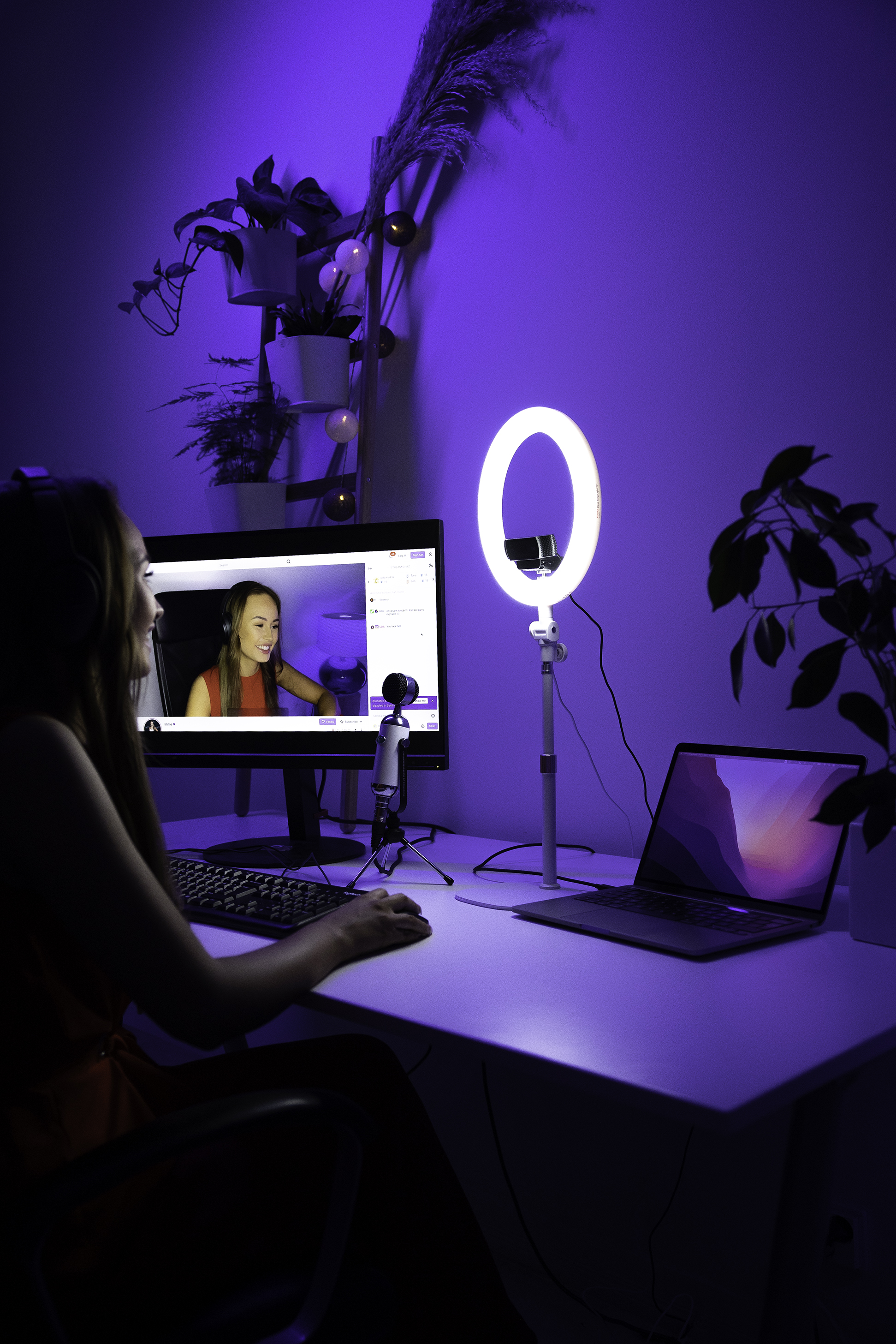 Frau streamt. Ringlicht, Monitor, Laptop und Mikrofon stehen auf dem Schreibtisch.