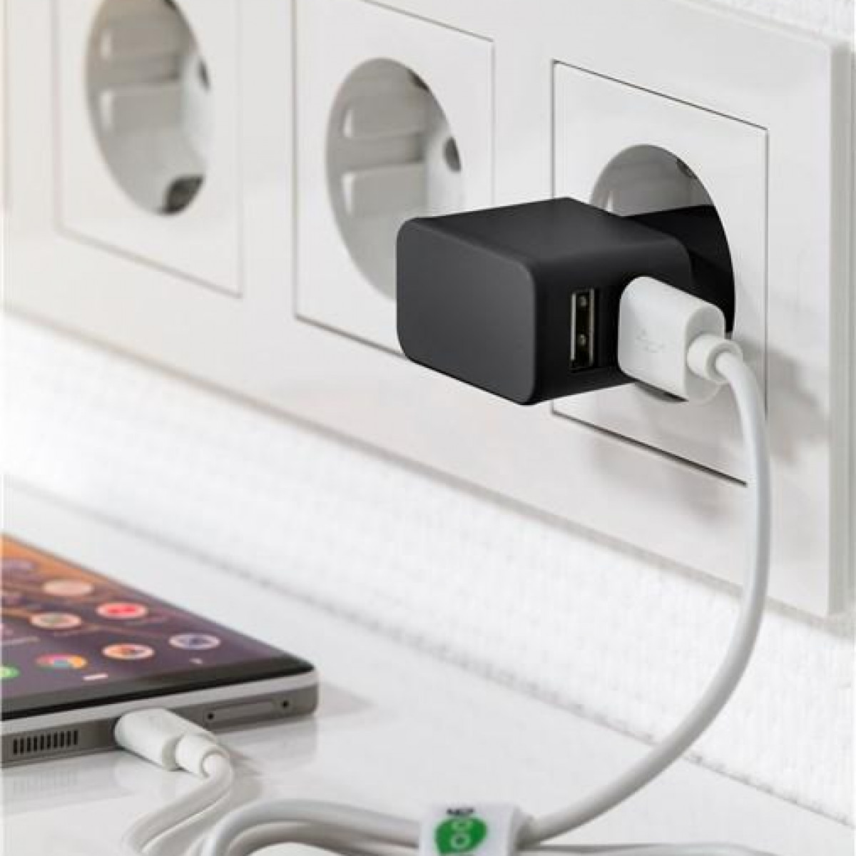 Ein schwarzes Ladegerät, das in eine Steckdose gesteckt wird, mit einem Telefon, das geladen wird. Ein weißes Kabel ist angeschlossen.