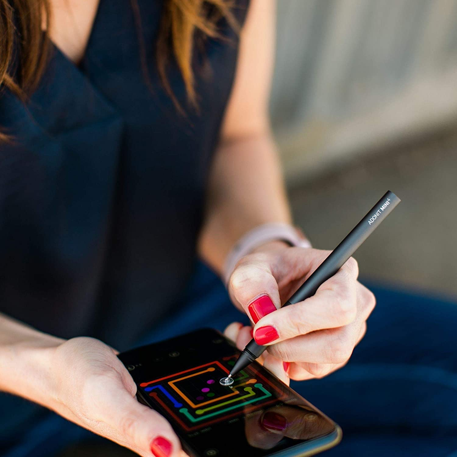 Una persona tiene in mano una penna stilo nera e la usa su uno smartphone. Smalto rosso visibile.
